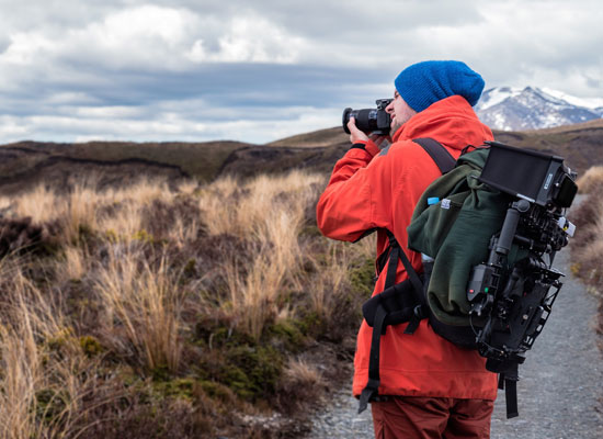 Fotógrafo con equipo profesional capturando paisajes en un sendero montañoso.