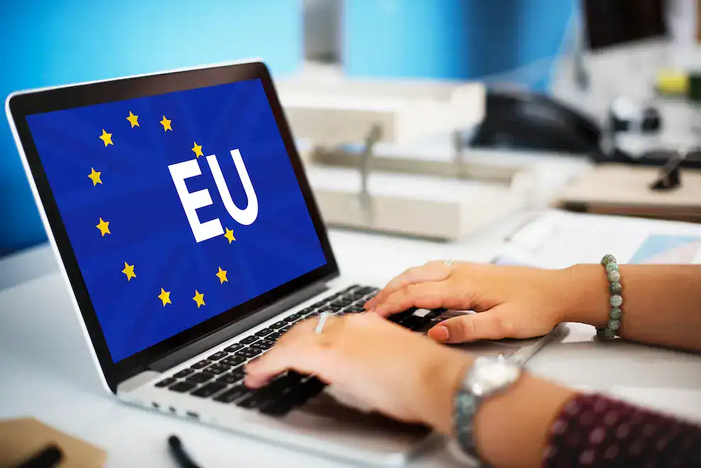 Persona usando un ordenador portátil que muestra la bandera de la Unión Europea, simbolizando la solicitud digital de ayudas y subvenciones europeas para emprendedores.