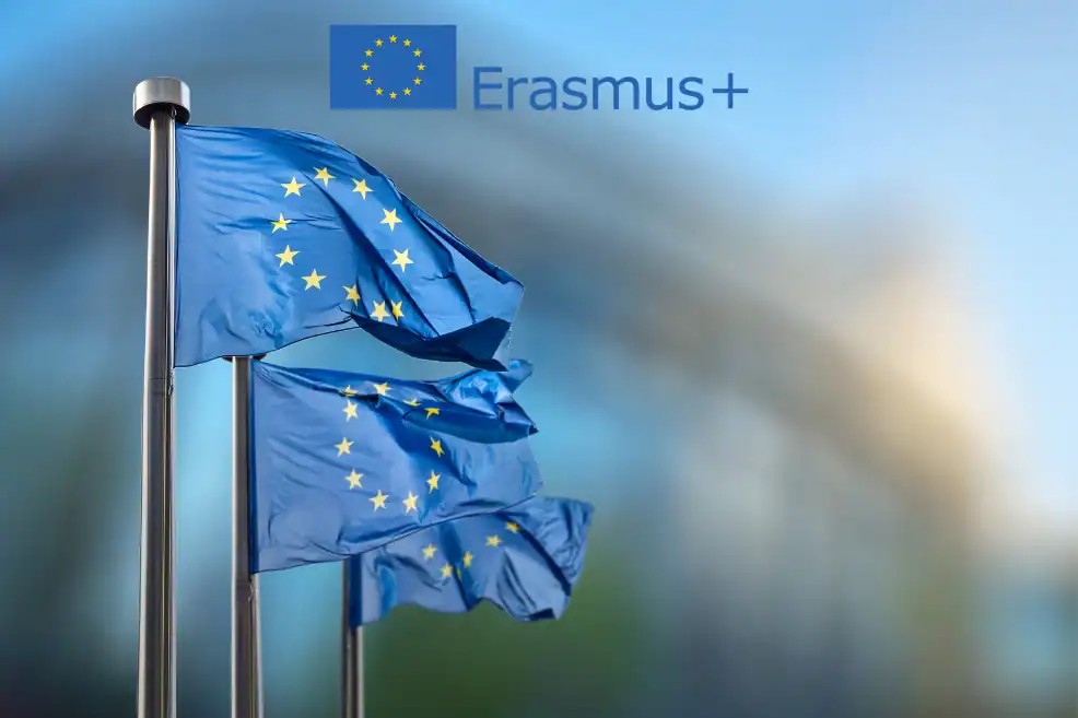 Banderas de la Unión Europea ondeando y logo de Erasmus+, simbolizando financiación europea para proyectos educativos y movilidad.